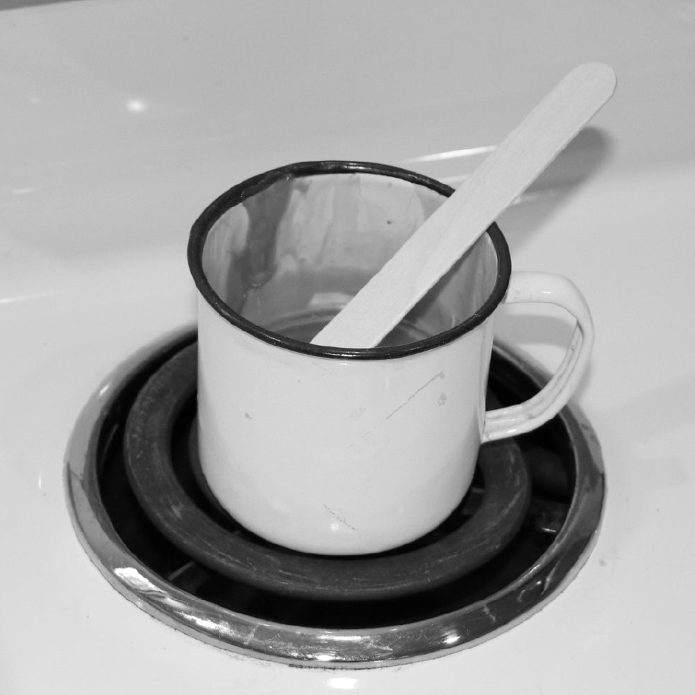 Photo of enamel mug filled with hot wax on stove top.