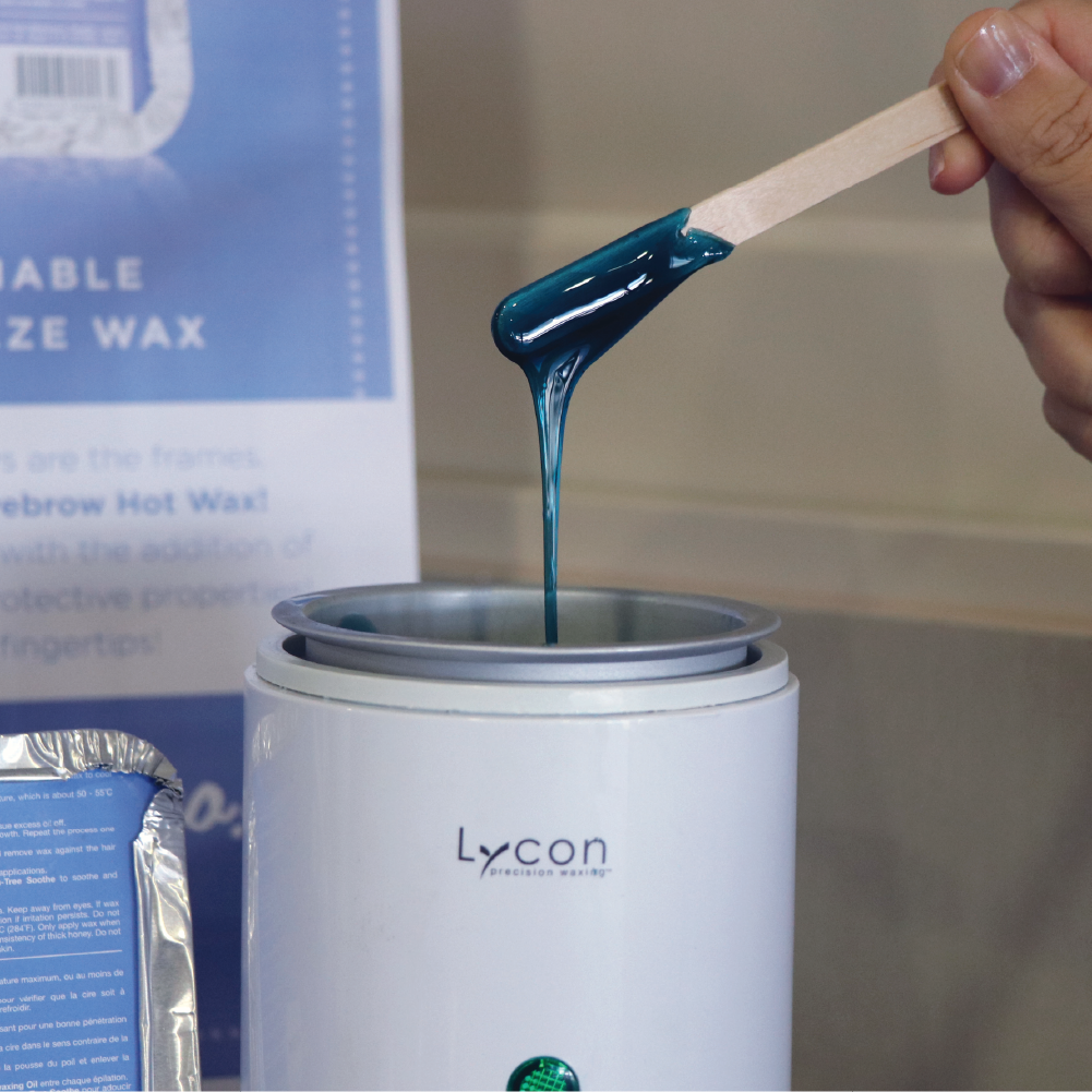 Photo of LYCOjet Eyebrow Hot Wax in LYCON Baby Heater with hand holding spatula dripping wax into heater.