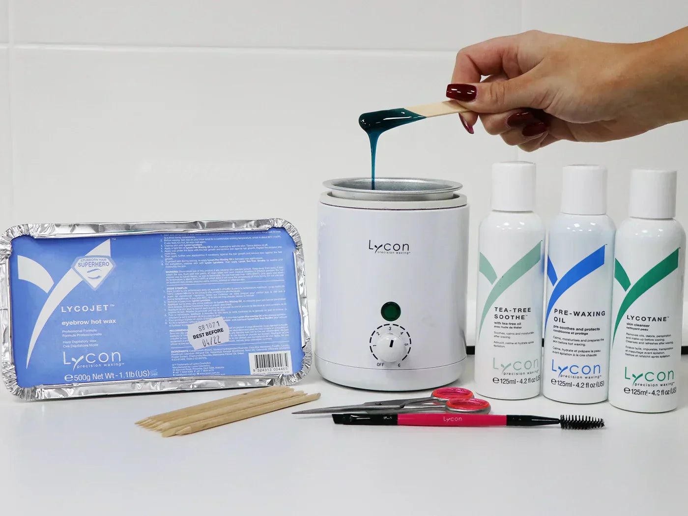 A photo of LYCON's LYCOjet Eyebrow Hot Wax alongside a hand using a spatula into melted wax in a wax heater